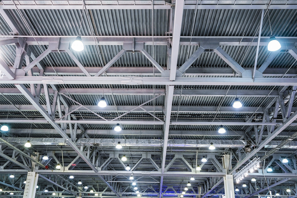 ceiling of industrial building with LED-retrofitted round high bay lights and steel trusses below a corrugated metal roof