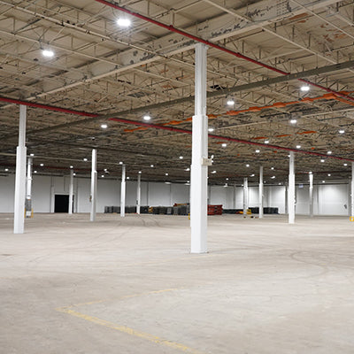 Large empty industrial warehouse with LED high bay retrofit lighting installed at 30-foot ceiling height providing bright uniform illumination across concrete floor demonstrating energy-efficient commercial lighting upgrade for manufacturing and distribution facilities